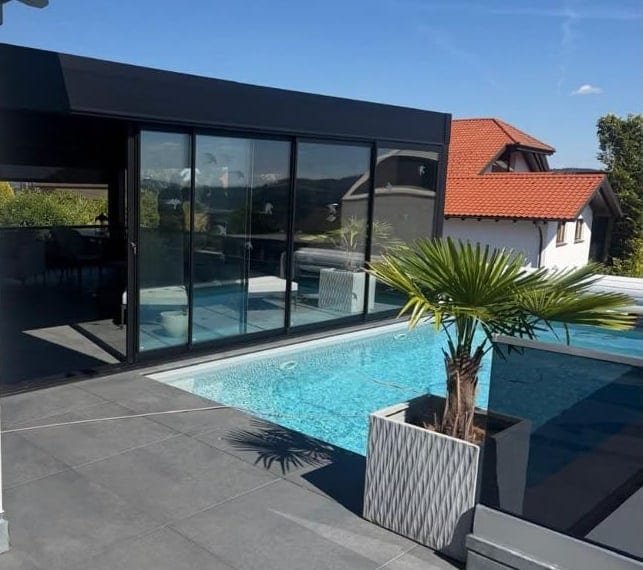 Verglaster Outdoor Room mit anthrazitfarbenem Dach direkt am Pool