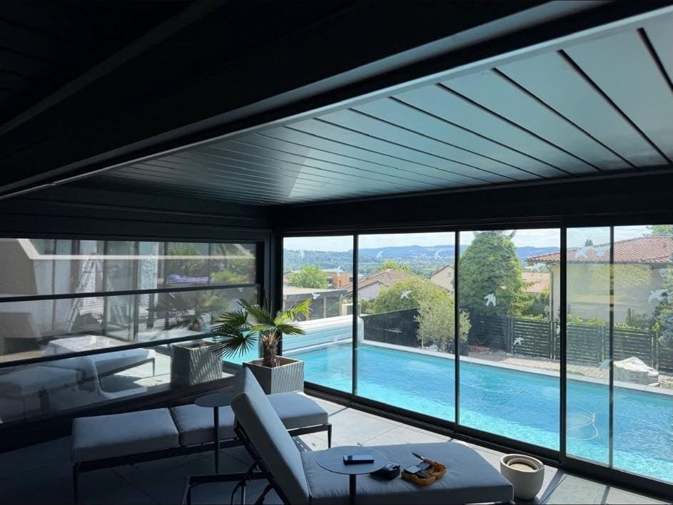 Blick aus einem verglasten Outdoor Room mit geschlossenem Lamellendach über den Pool ins Tal