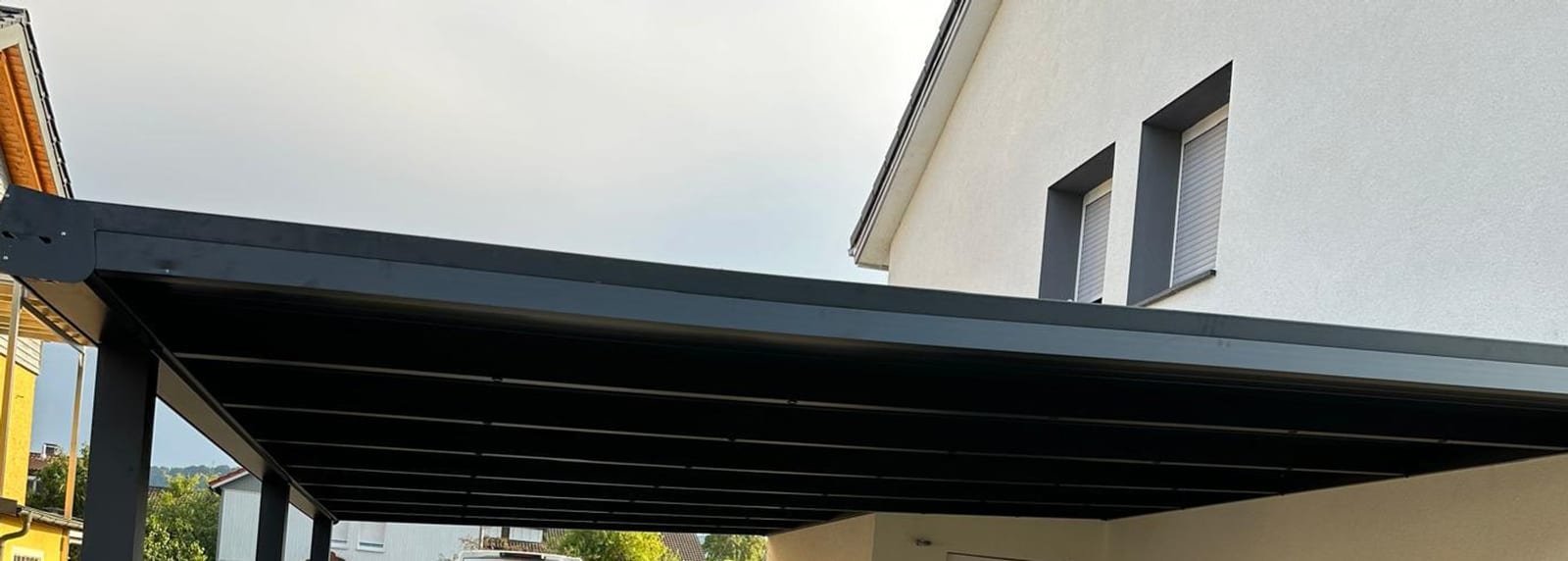 Untersicht eines anthrazitfarbenen Carportdachs an einem Wohnhaus, kurz nach der Montage