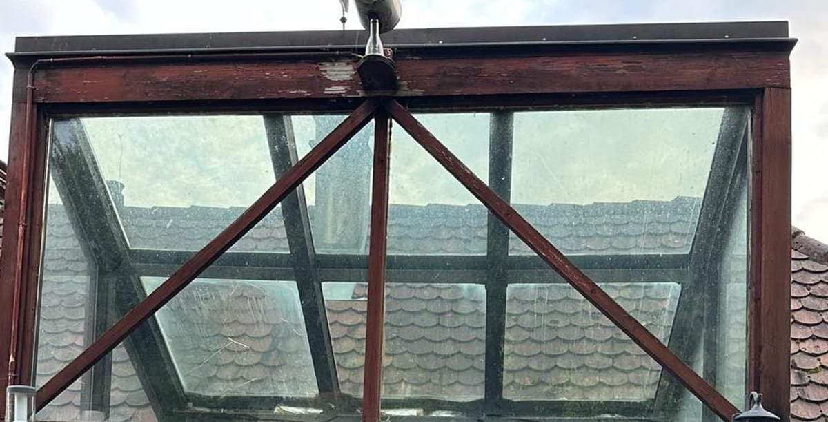 Alter Dachaufbau aus dunklem Holz mit Kreuzstrebe unter dem Glasdach