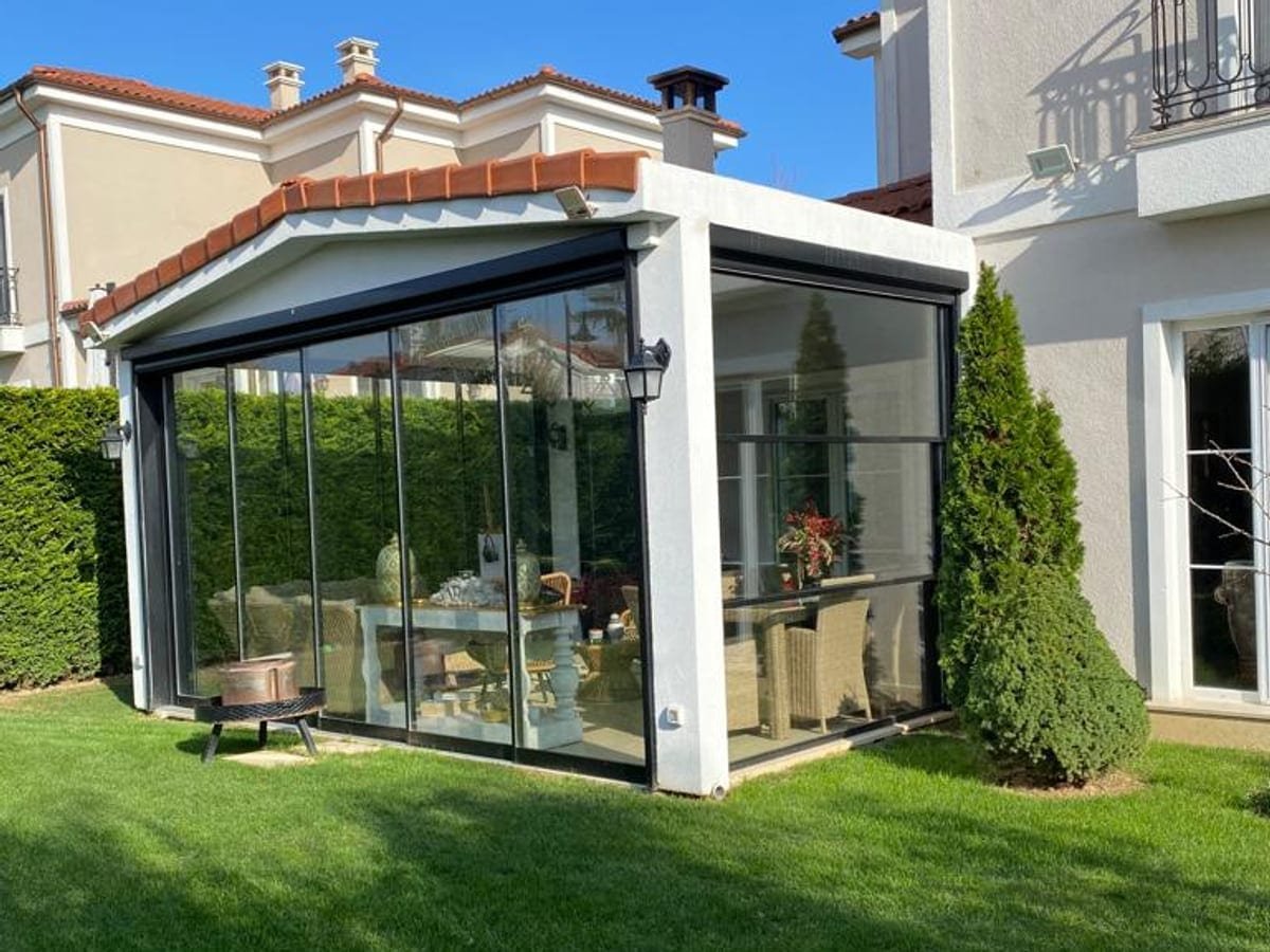 Verglaster Wintergarten an einem Wohnhaus, davor Rasen